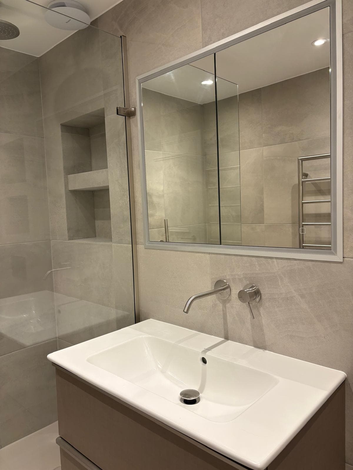 Contemporary bathroom renovation London — wall-hung vanity with illuminated mirror cabinet and stone-effect tiles