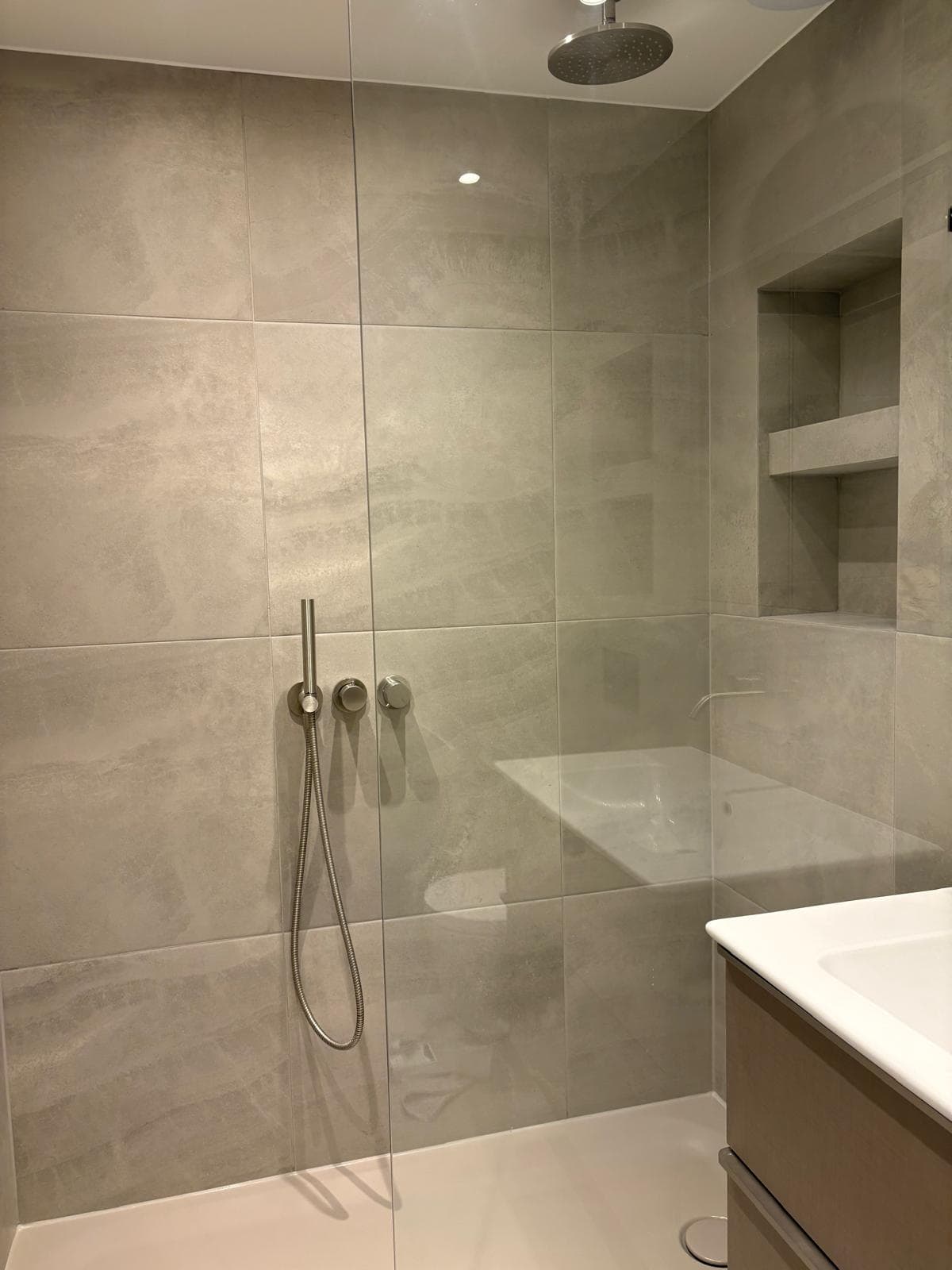 Frameless walk-in wet room with ceiling-mounted rain head and recessed niche shelving, London