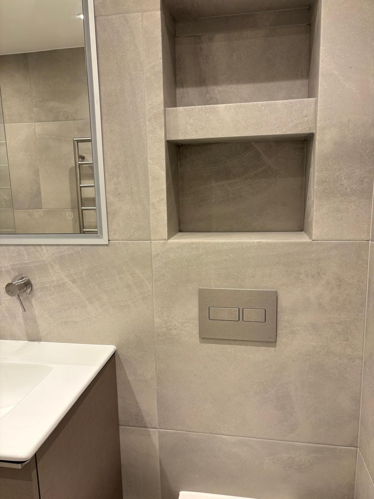 Stone-effect tiled bathroom with concealed wall-hung WC and recessed niche, London renovation